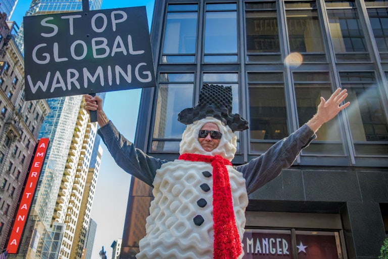 A protester dressed as a snowman holds a sign reading "Stop Global Warming."