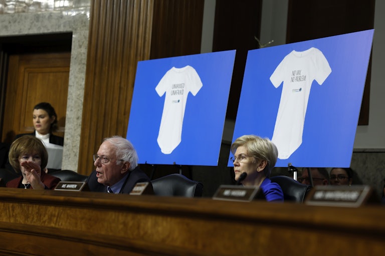 Bernie Sanders and Elizabeth Warren sit in front of posters showing anti-vaccine onesies during Robert F. Kennedy Jr.’s confirmation hearing