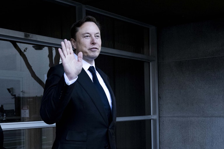 Elon Musk holds a hand up in greeting
