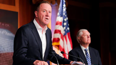 Senator Eric Schmitt leans on a podium while speaking during a press conference