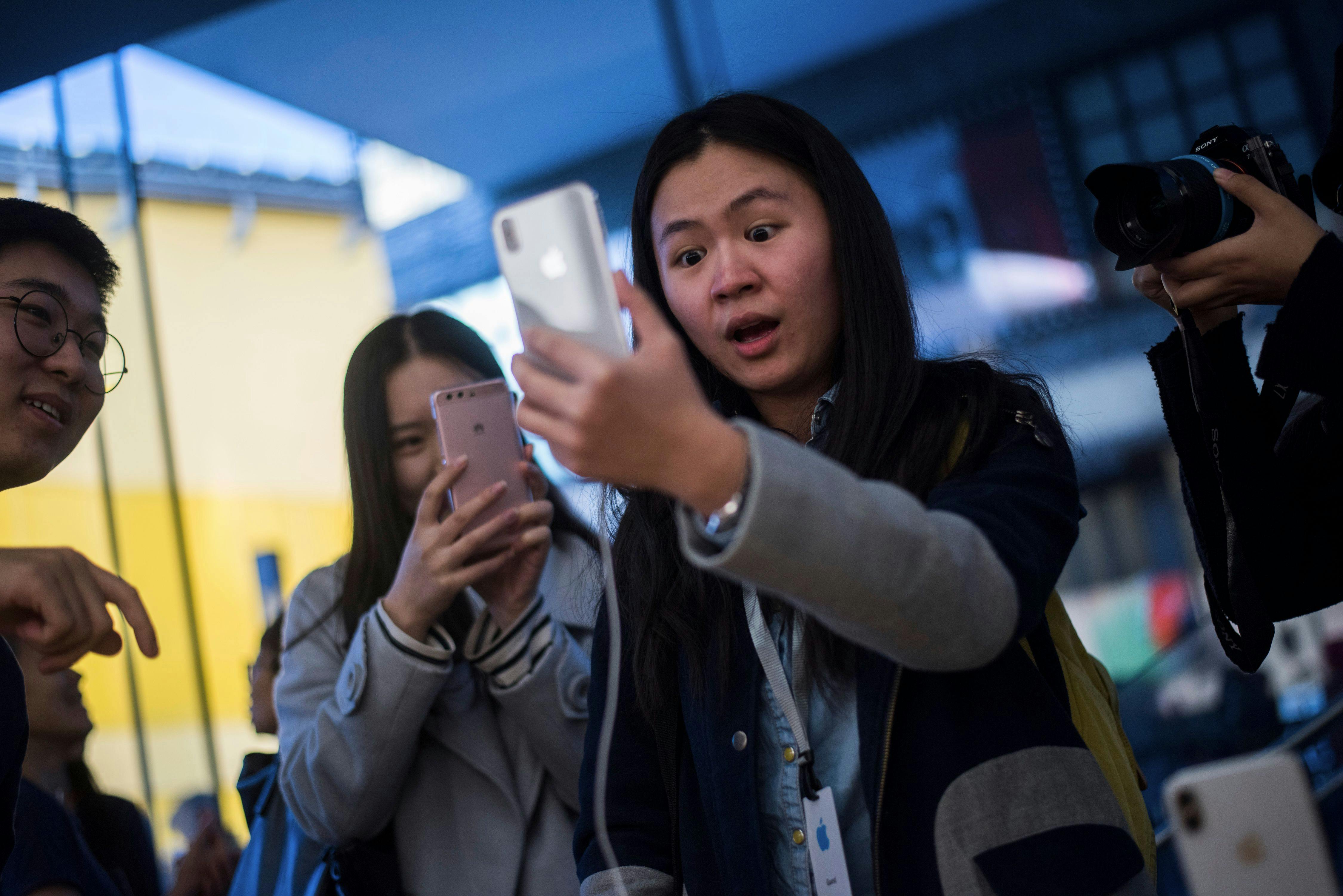 A woman enthusiastically gawks at her iPhone amid a crowd of onlookers.