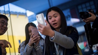 A woman enthusiastically gawks at her iPhone amid a crowd of onlookers.