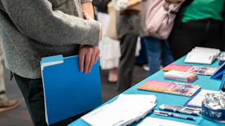 A jobseeker holds a folder while speaking with a recruiter at a booth.