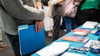 A jobseeker holds a folder while speaking with a recruiter at a booth.
