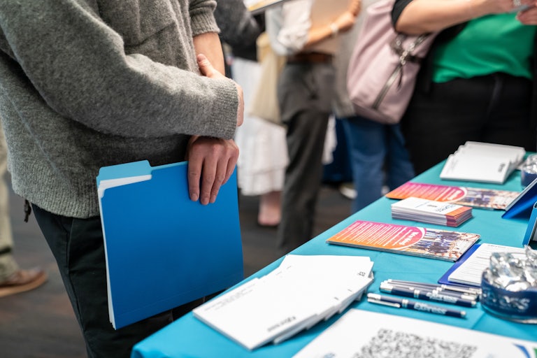 A jobseeker holds a folder while speaking with a recruiter at a booth.
