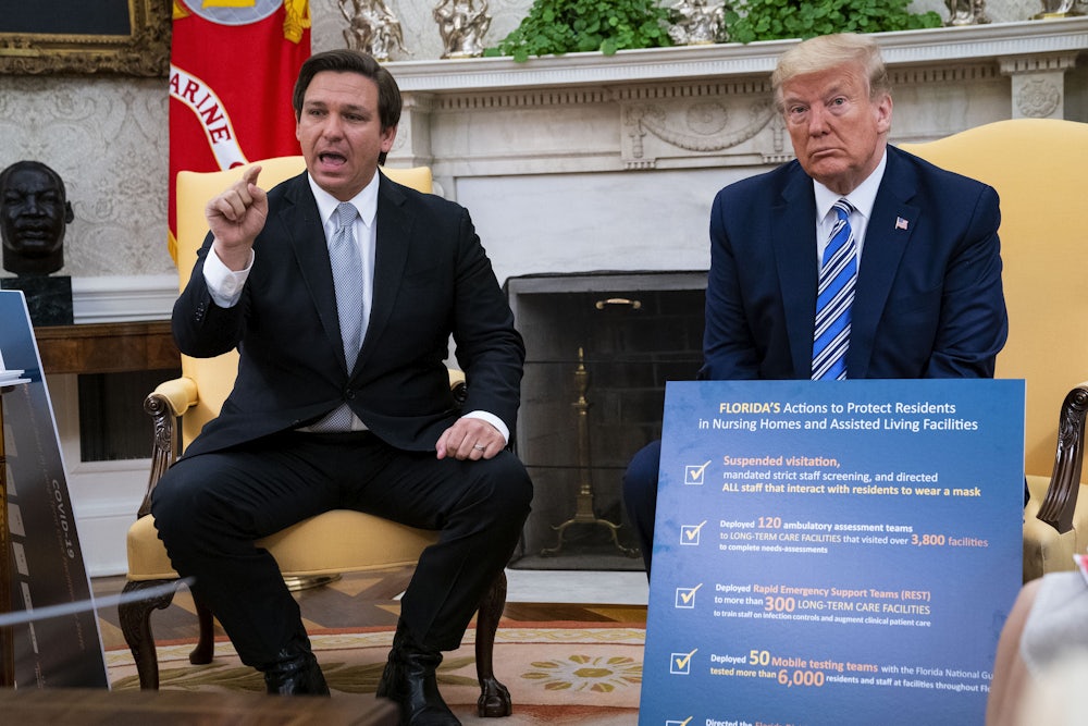 Florida Governor Ron DeSantis gesticulates while speaking as President Donald Trump looks on.