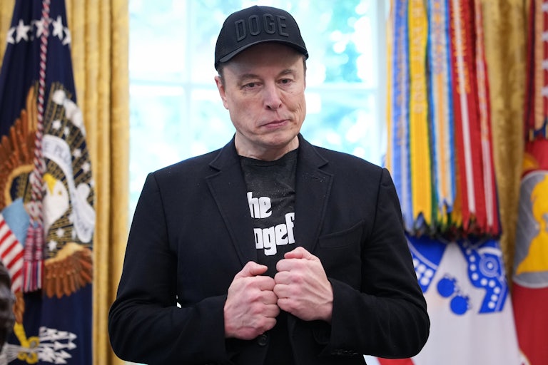 Elon Musk wears a black bazler over a shirt that says "The Dogefather."