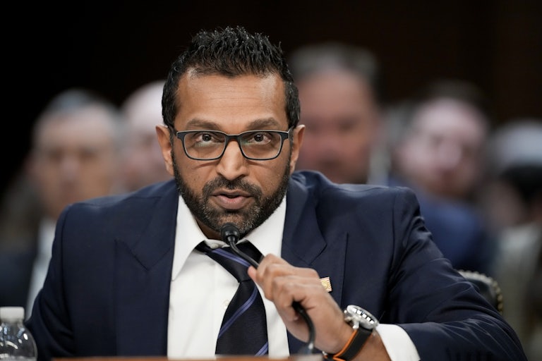 FBI Director Kash Patel leans forward in a congressional hearing to grab the mic and speak.