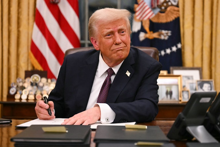 Donald Trump smiles weirdly as he signs an executive order at his desk in the Oval Office