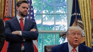 JD Vance stands with his arms crossed and looks down at Donald Trump, who sits at his desk in the Oval Office