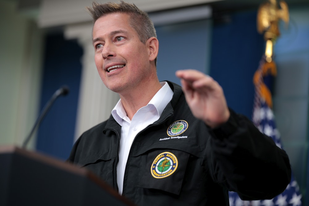 Sean Duffy gesticulates while standing at a lectern, wearing a black jacket with badges.