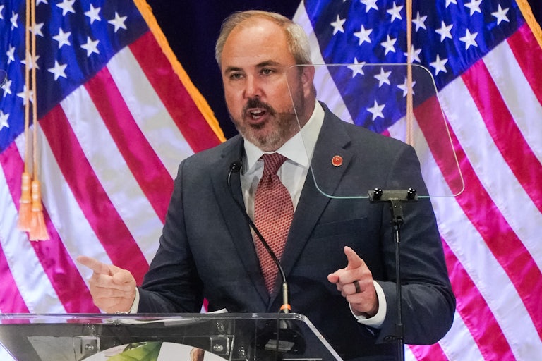 RNC Chair Joe Gruters speaks at a lectern in front of U.S. flags.