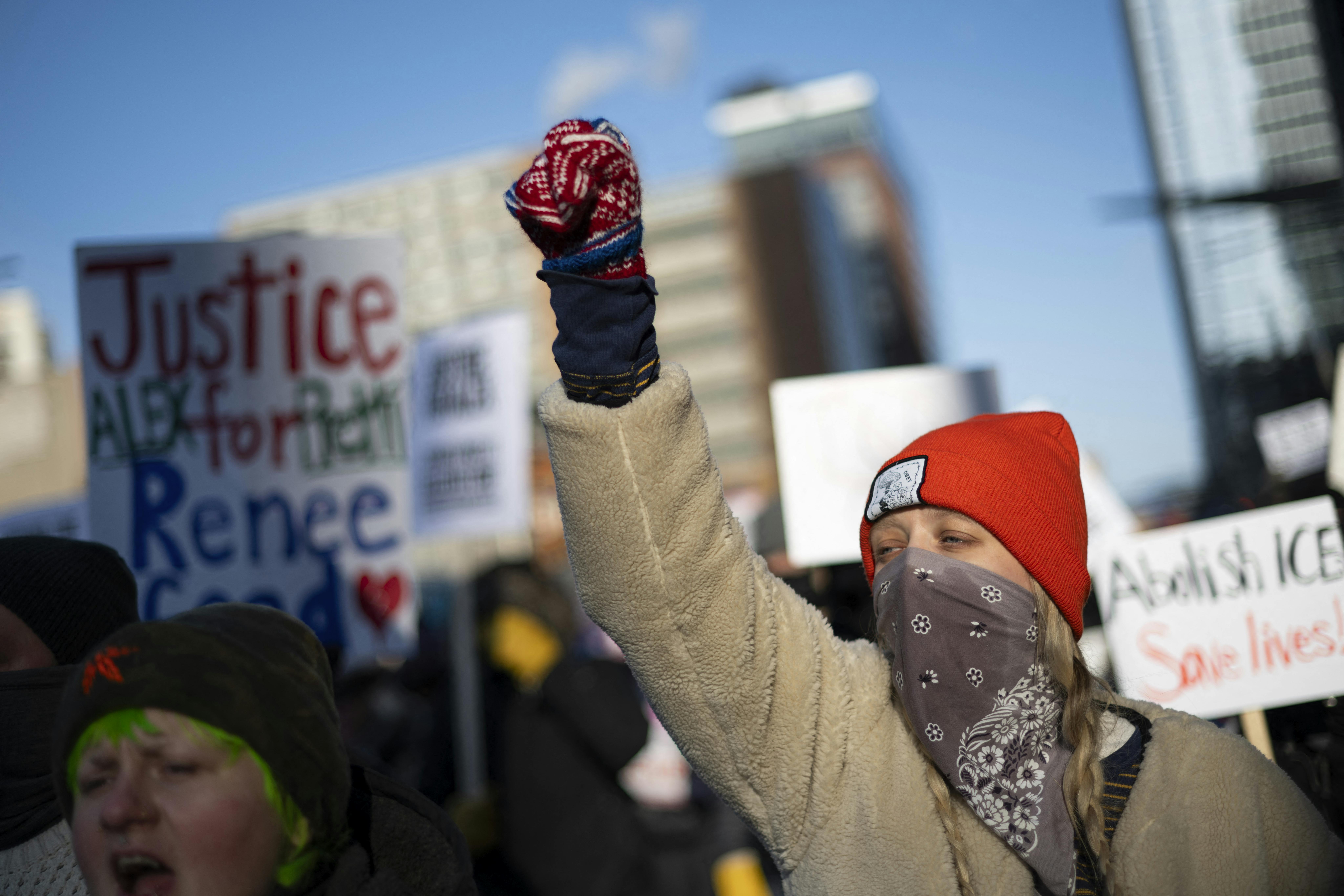 Protesters and signs are seen with one protester in the foreground, holding up a gloved fist.