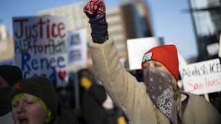 Protesters and signs are seen with one protester in the foreground, holding up a gloved fist.