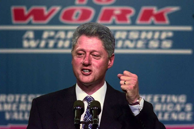Bill Clinton raises his fist in front of a sign that reads “Welfare to work.”