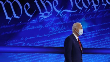 Joe Biden stands in front of a background reading “We the People.”