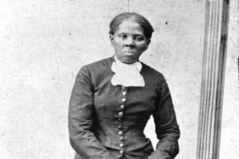 black and white photo of Harriet Tubman resting her hands on the back of a chair.