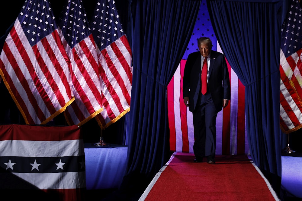 Trump walks through curtains with American flags draped everywhere.