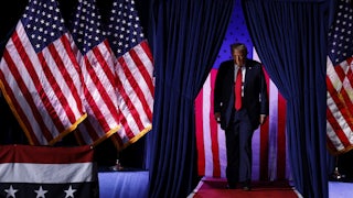 Trump walks through curtains with American flags draped everywhere.