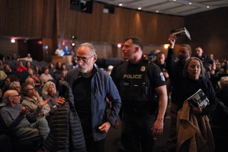 A police officer escorts two older people outside Lawler’s packed town hall. Another man following them holds up a sign that reads "Impeach Trump."