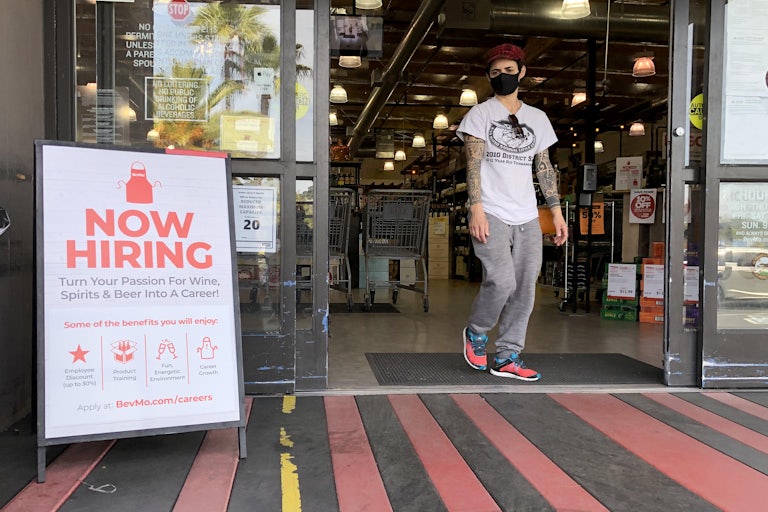A masked customer walks past a "Now Hiring" sign outside a BevMo store in Larkspur, California.