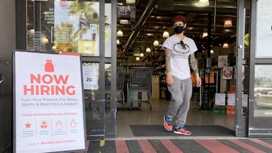A masked customer walks past a "Now Hiring" sign outside a BevMo store in Larkspur, California.