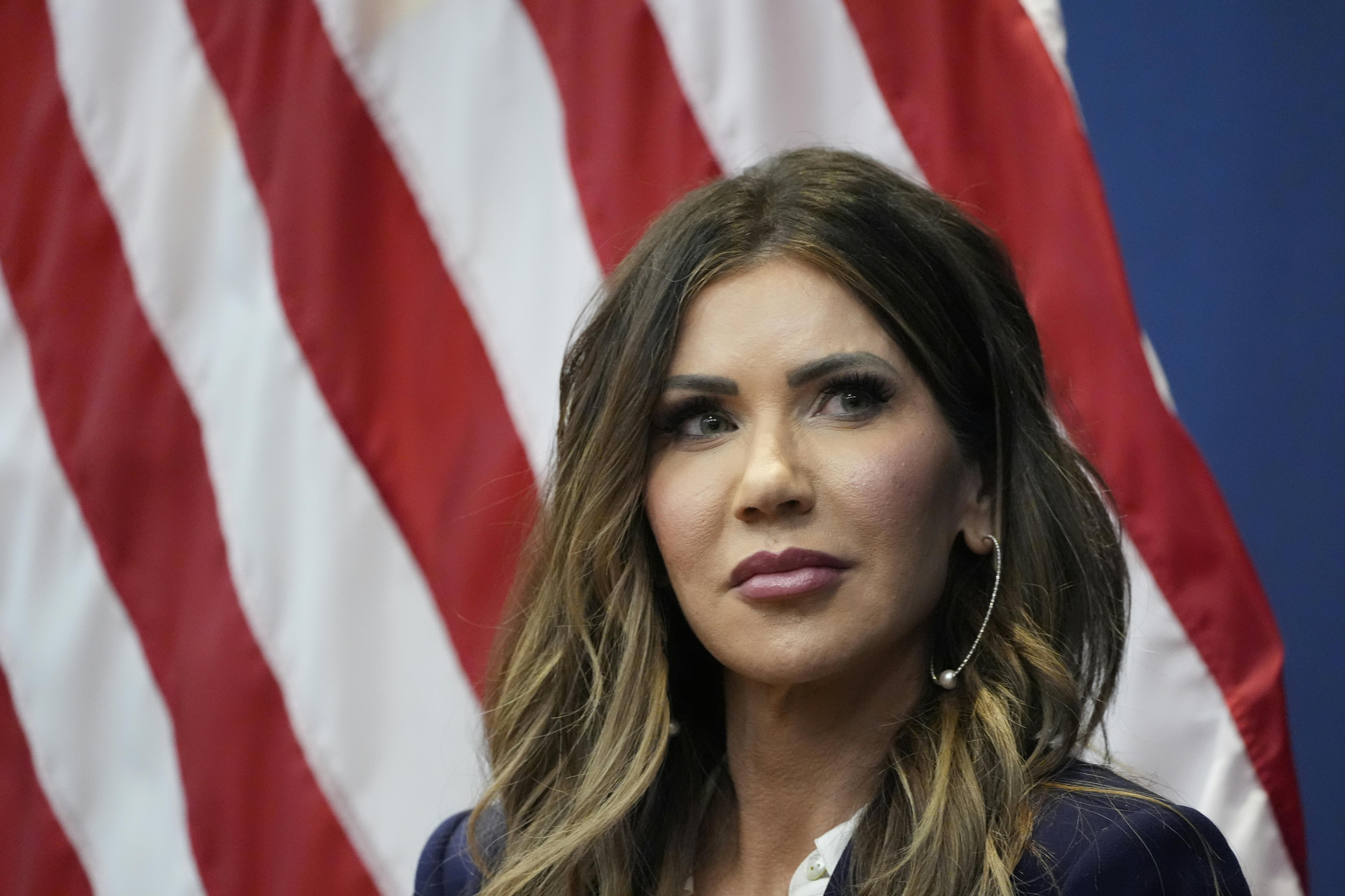 Homeland Security Secretary Kristi Noem sits in front of an American flag