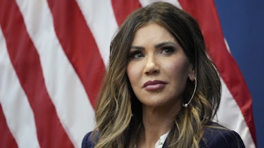 Homeland Security Secretary Kristi Noem sits in front of an American flag