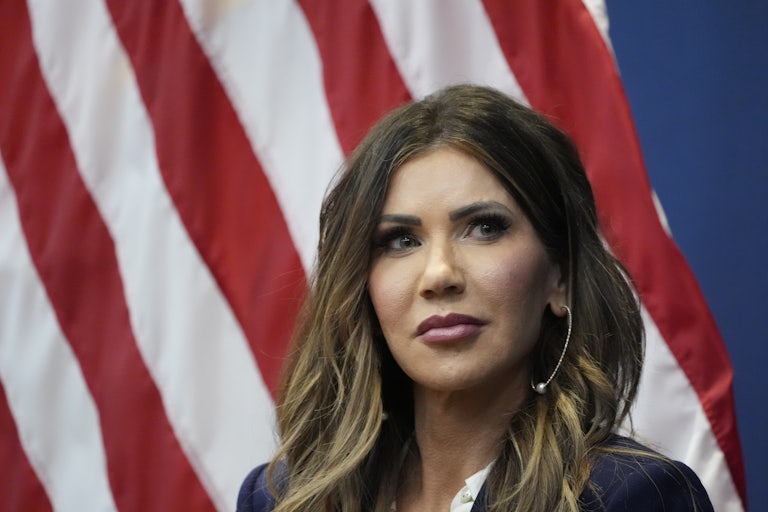 Homeland Security Secretary Kristi Noem sits in front of an American flag