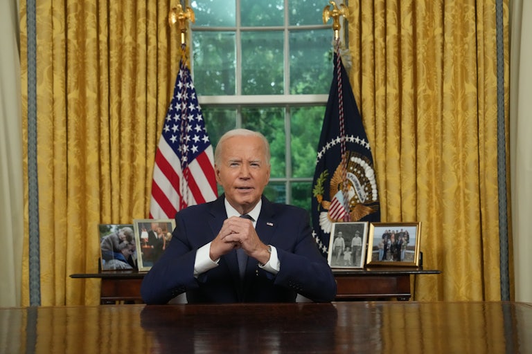 Joe Biden sits with his hands folded on his desk in the Oval Office