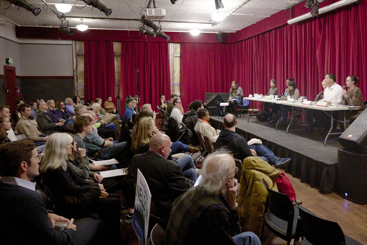 Onstage, from right: Katie Wilson, Mayor Bruce Harrell, and other candidates at a forum