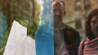 People watching a television replay scenes from the September 11, 2001 attack on the World Trade Center, reflected in the window of a store, February 20, 2002 in New York City.