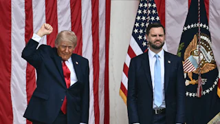 Donald Trump raises his fist and JD Vance stands with his arms hanging limply. A large U.S. flag is behind them.