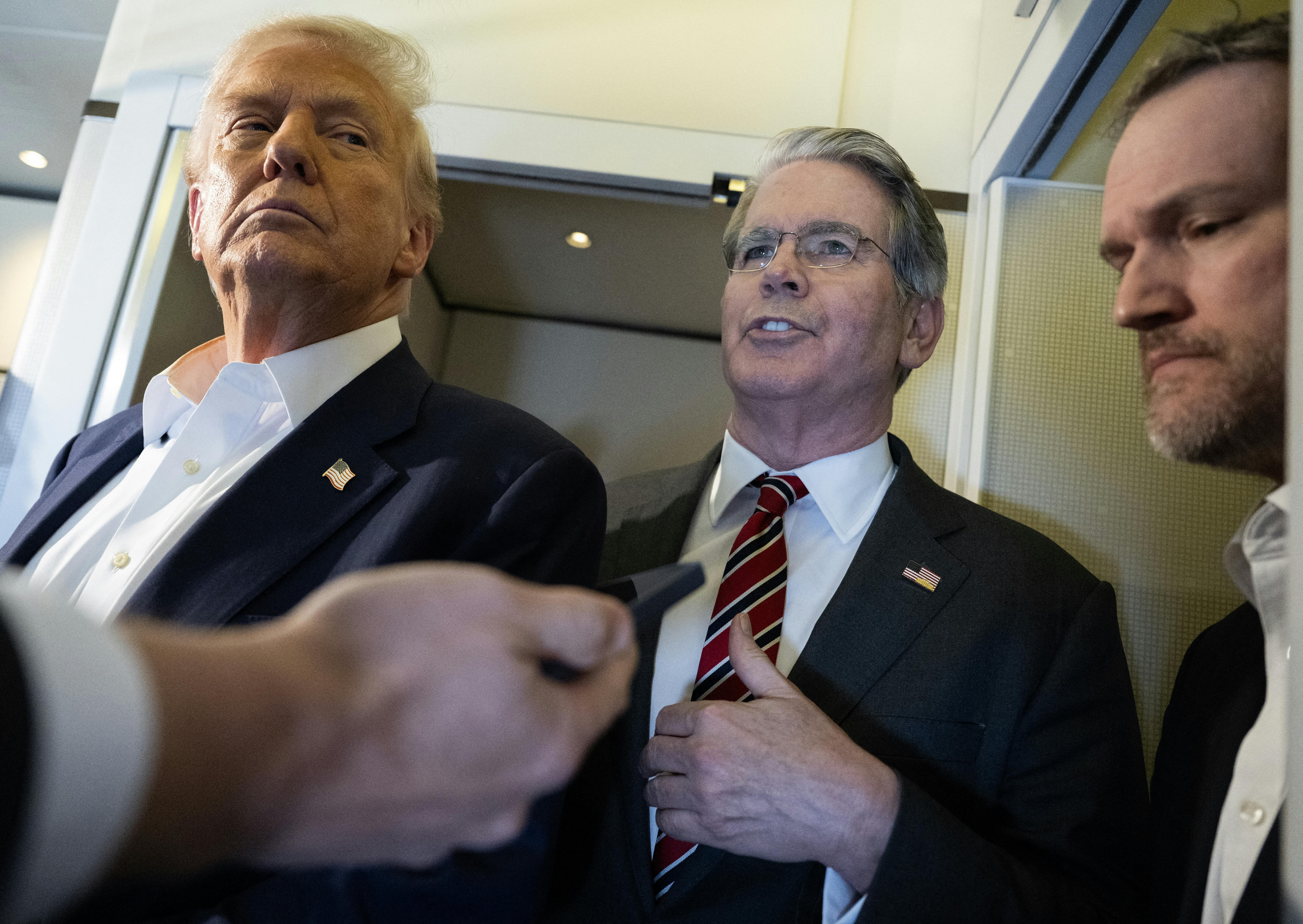 Treasury Secretary Scott Bessent speaks to reporters on Air Force One while standing between Donald Trump and Trade Representative Jamieson Greer