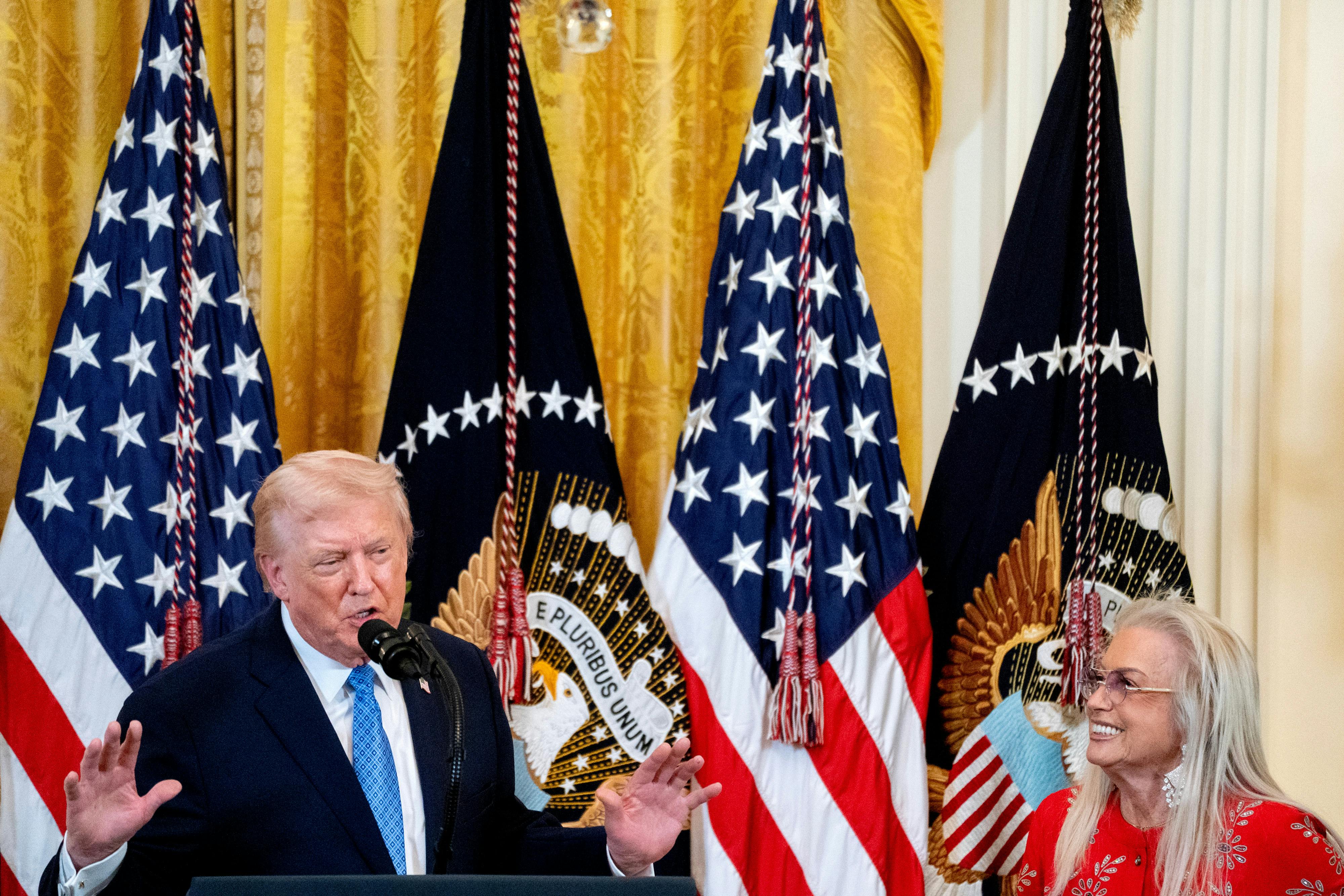 Donald Trump speaks into a mic while Miriam Adelson smiles and listens.