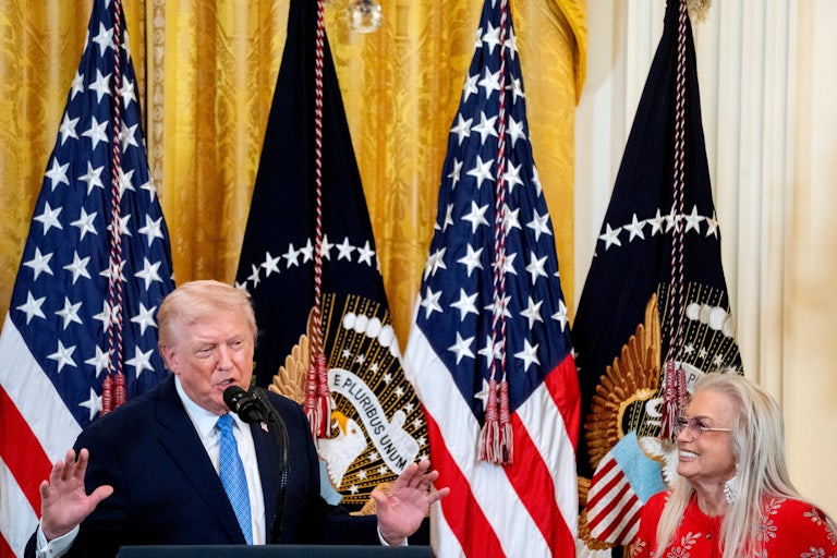 Donald Trump speaks into a mic while Miriam Adelson smiles and listens.