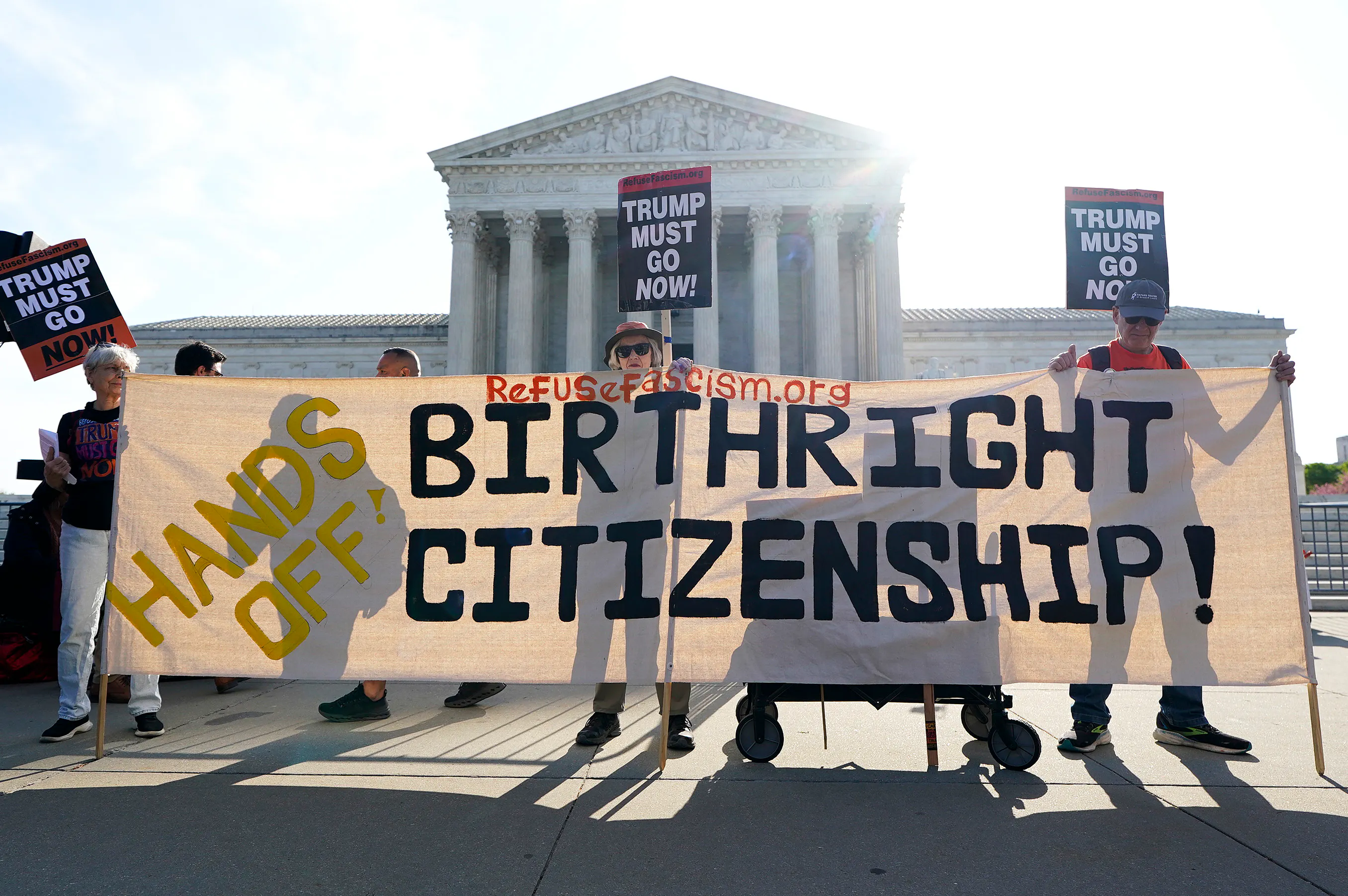 People outside the Supreme Court hold up signs reading "Trump must go now" and "Hands off Birthright Citizenship."
