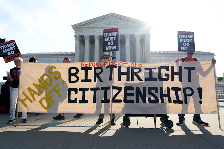 People outside the Supreme Court hold up signs reading "Trump must go now" and "Hands off Birthright Citizenship."