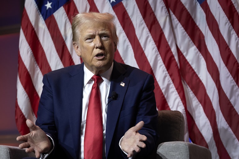 Donald Trump, seated, speaks and splays his hands outward