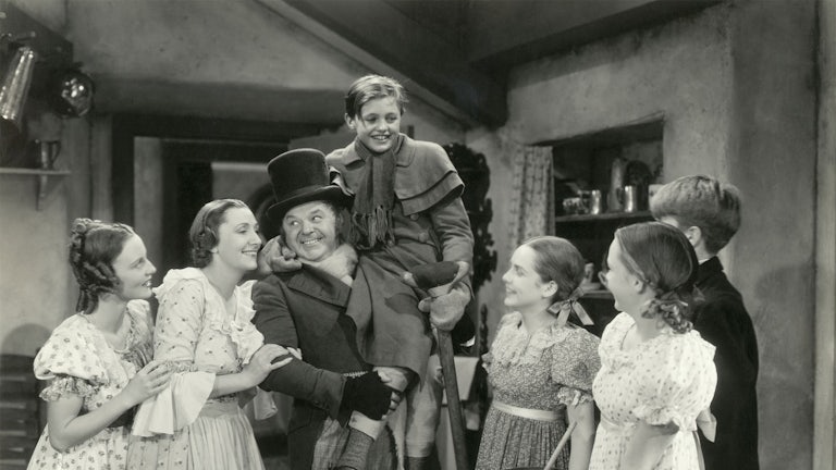 In this scene from the 1938 motion picture A Christmas Carol, Bob Cratchit hoists Tiny Tim in the air as his family looks on..