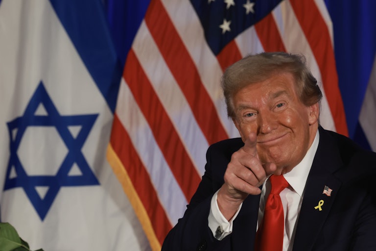 Donald Trump smiles and points while standing in front of an Israeli and a U.S. flag
