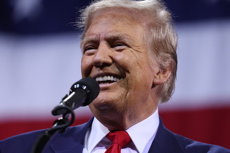 Donald Trump smiles while standing in front of a microphone at a campaign event