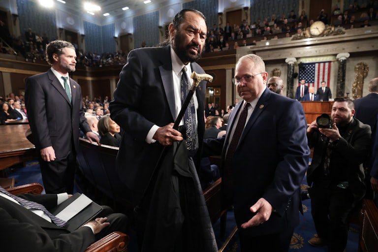 Representative Al Green holds his cane as another man escorts him out of the chamber during Trump’s speech.