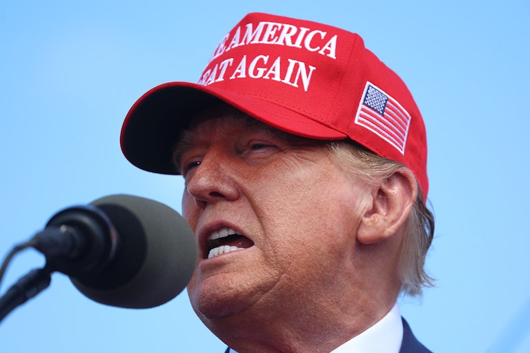 Trump wearking a Make America Great Again cap speaks into a mic outdoors