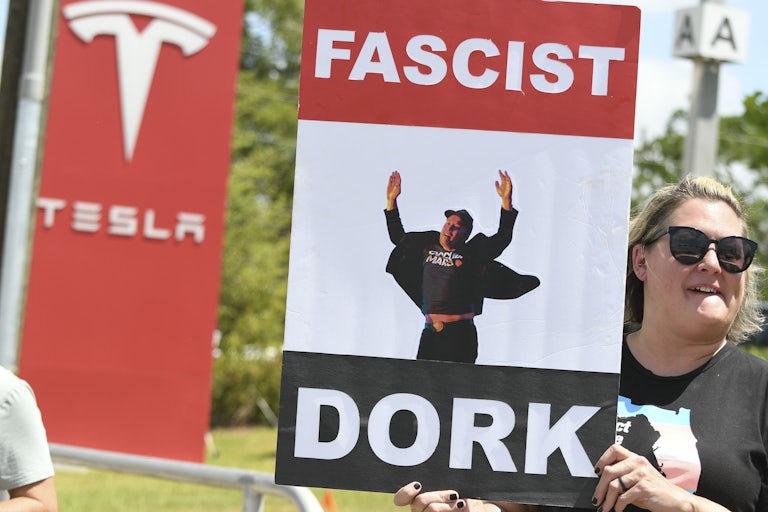 A person holds up a sign that has a photo of Elon Musk and the words "Fascist dork" on it during a protest outside a Tesla dealership