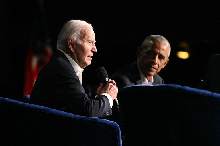 Joe Biden and Barack Obama sit in armchairs, as Biden speaks into a microphone and Obama looks at him
