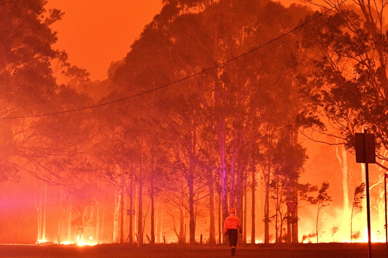 A firefighter walks past burning trees in New South Wales, Australia, in 2019.