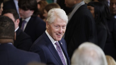 Former President Bill Clinton smiles and speaks while standing at a memorial service