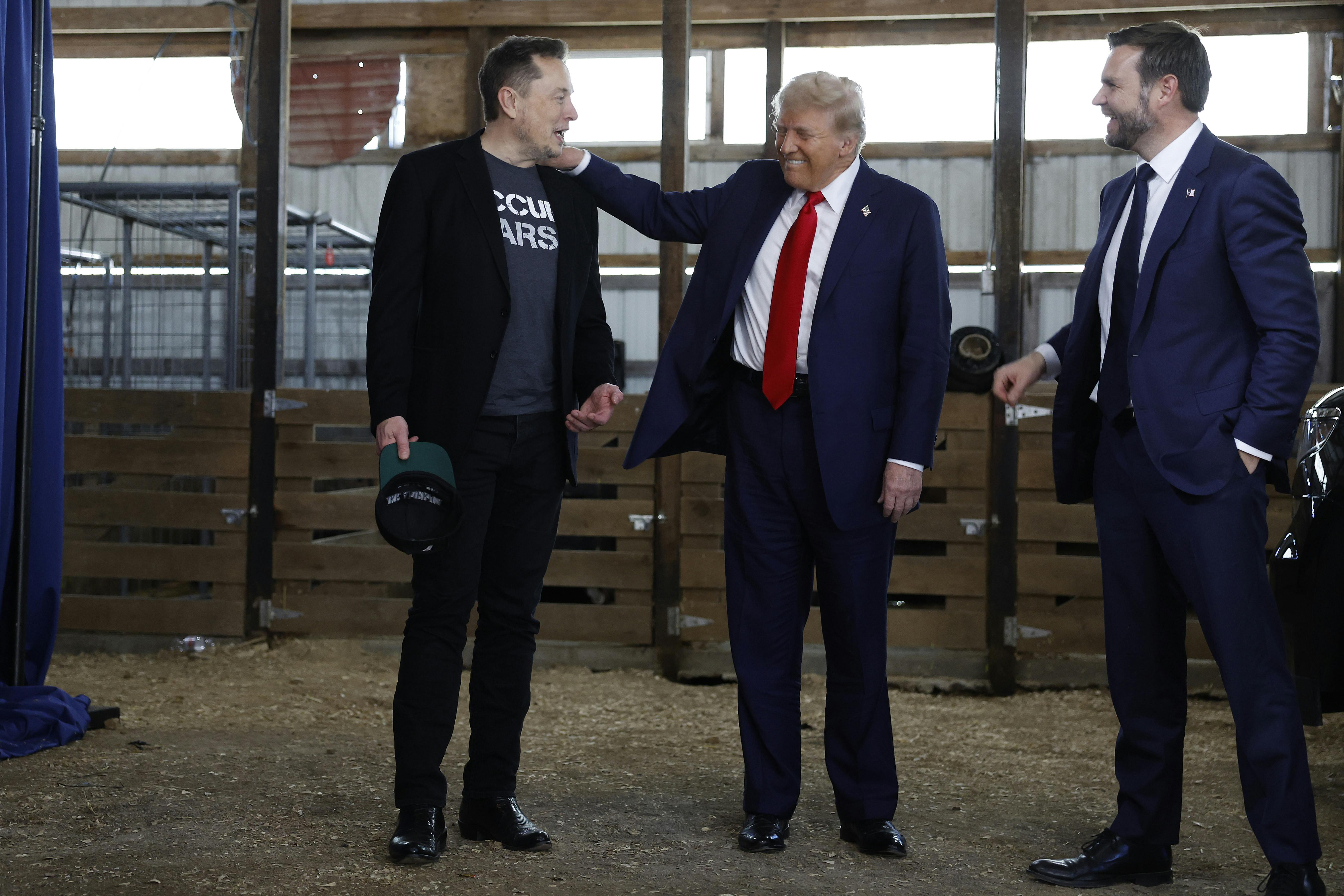 President Donald Trump visits with Elon Musk and JD Vance back stage during a campaign rally.