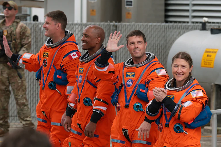 Artemis II astronauts wave while wearing their suits